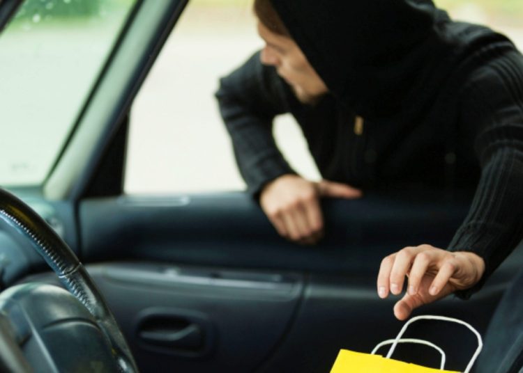 Transportation, crime and ownership concept - thief stealing shopping bag from the car